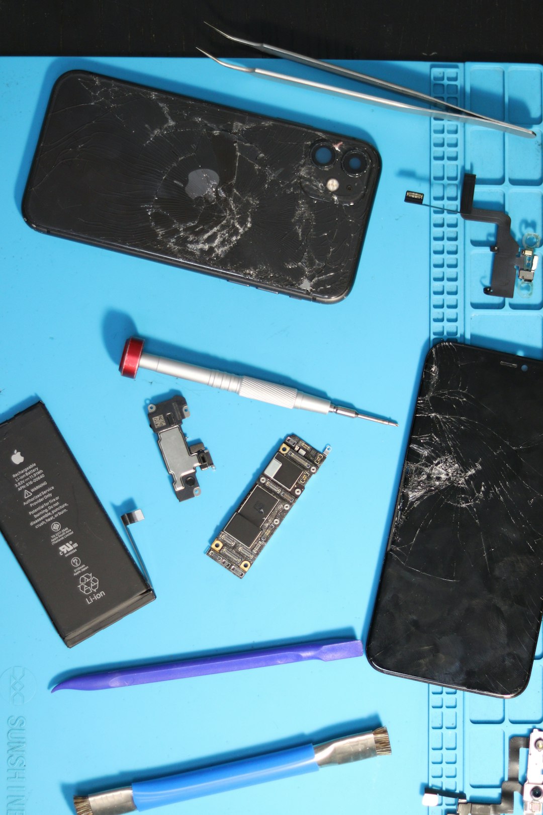 Broken iphones with repair tools on a blue mat.