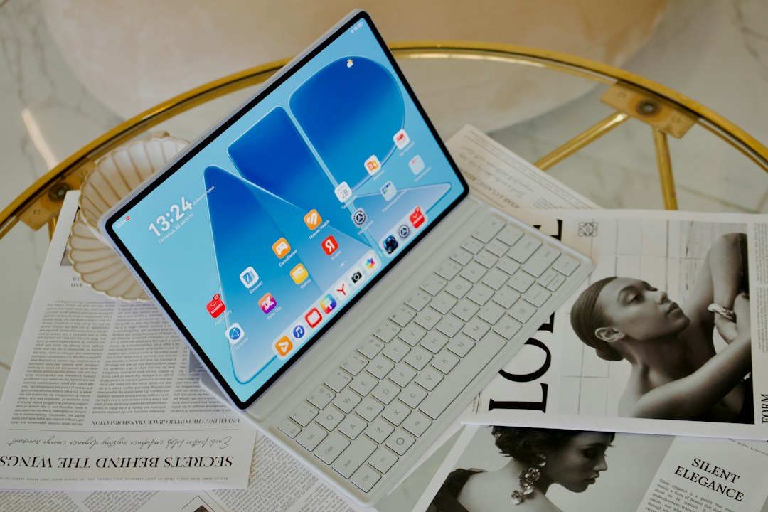 A tablet with a white keyboard cover on a glass table with magazines