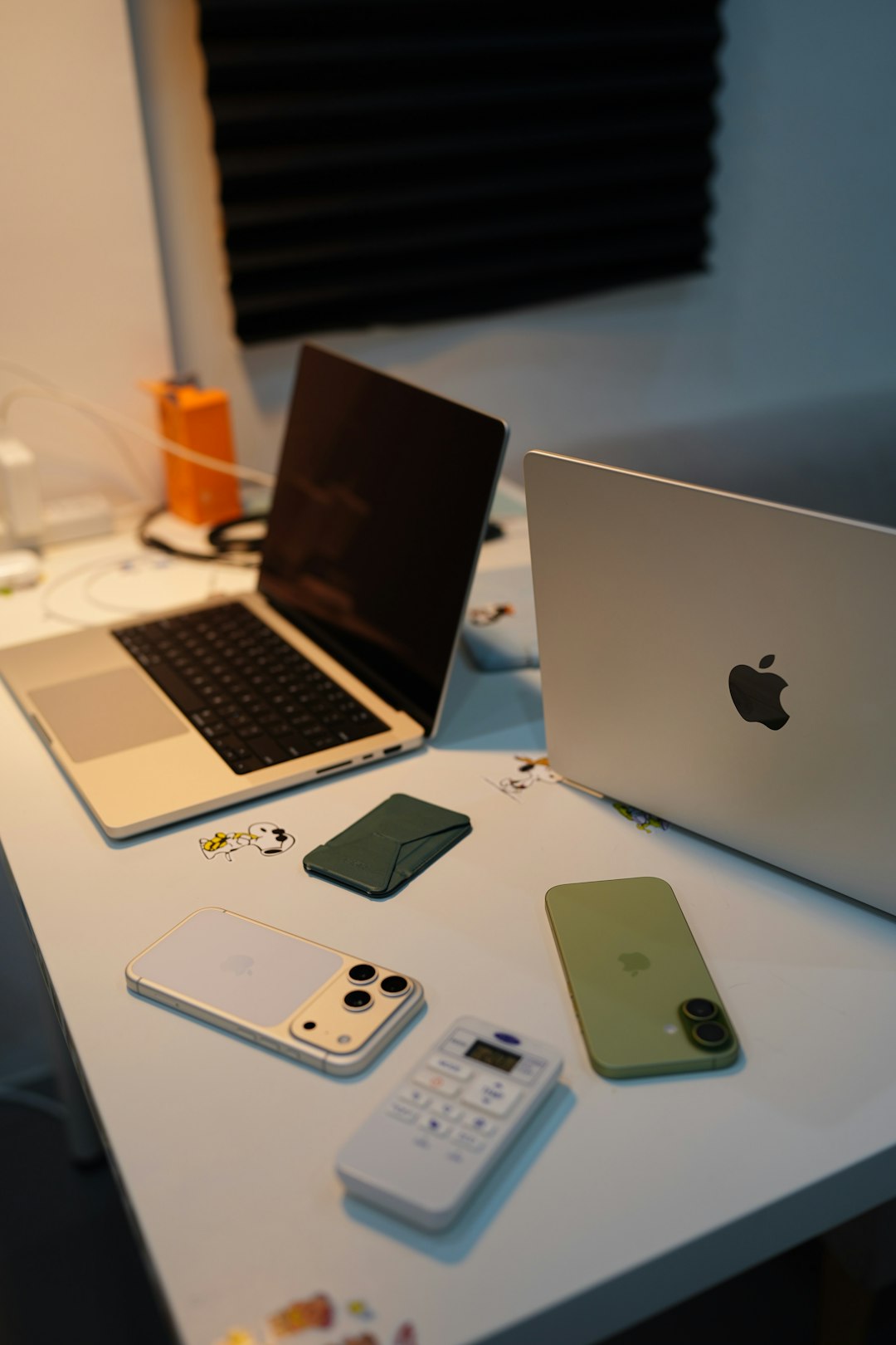 Two laptops, two smartphones, and a remote on a white desk with stickers